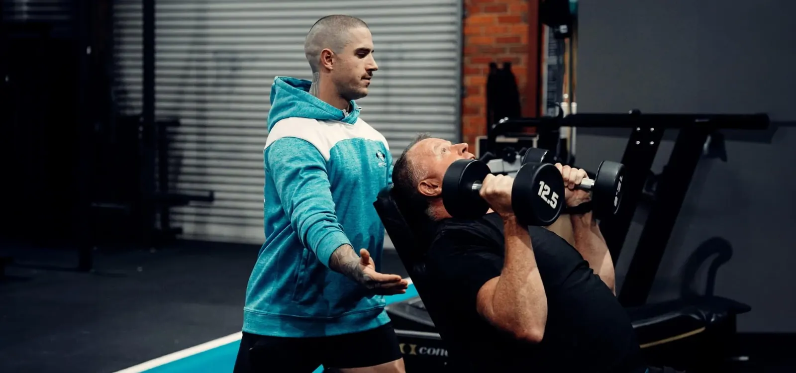 Coach spotting a client pressing dumbbells at East 2 West Fitness