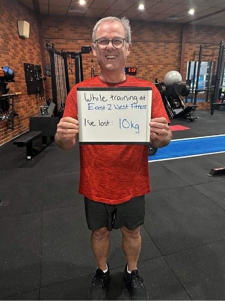 Client holding a whiteboard reading: while training at East 2 West Fitness I've lost 10 kg