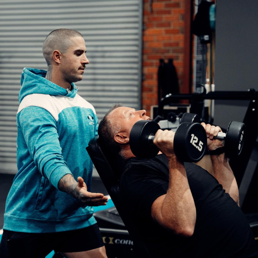 Trainer assisting with dumbbell press